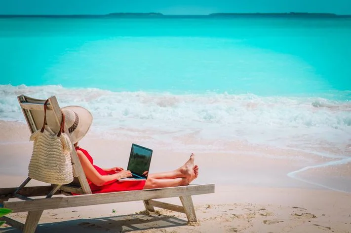 Woman sitting on a sun lounger on a beach with laptop